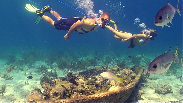 Two people snorkeling above a submerged boat with fish swimming nearby.