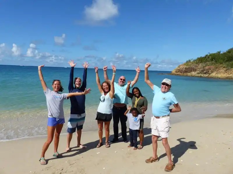Group of people joyfully posing on a sunny beach with blue sky.