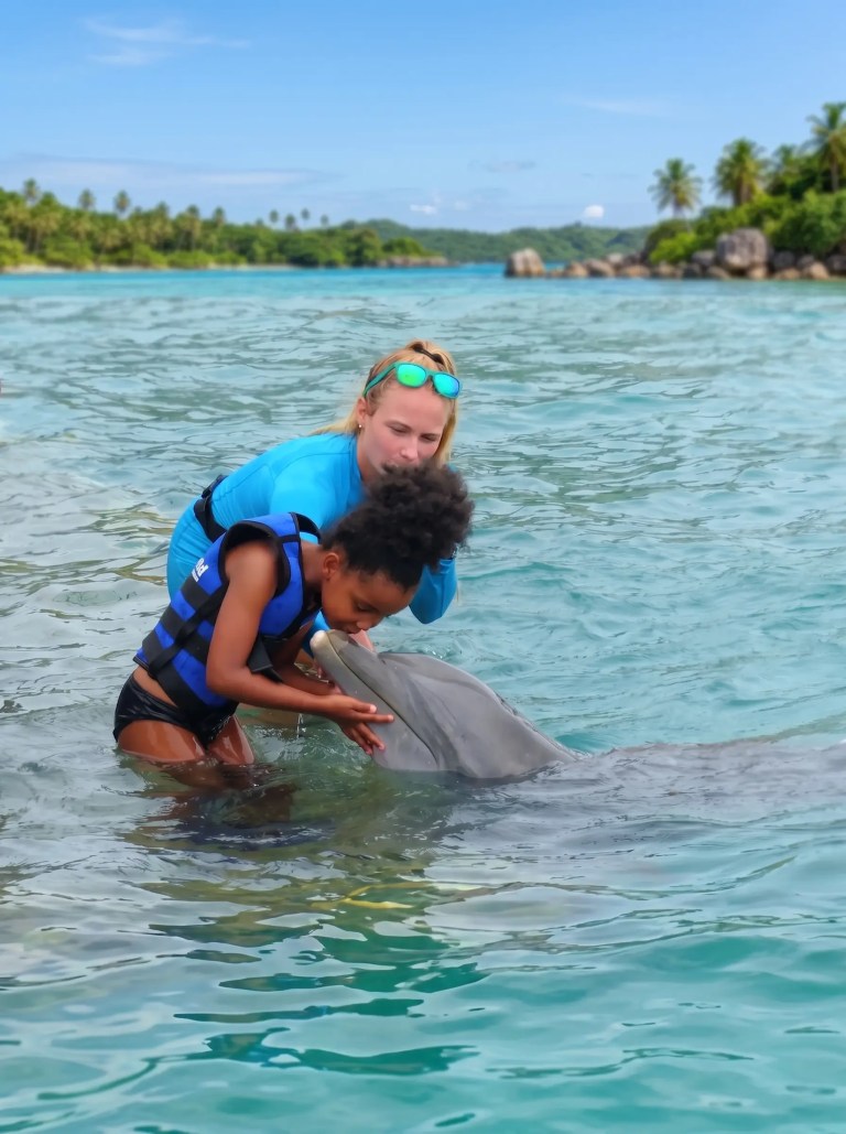 Child and adult in water interacting with a dolphin.