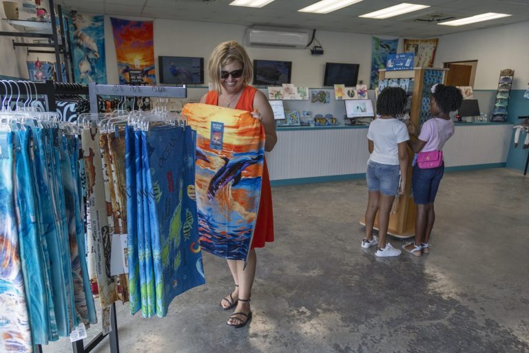 Woman in a store holding a colorful towel, with two girls browsing nearby.