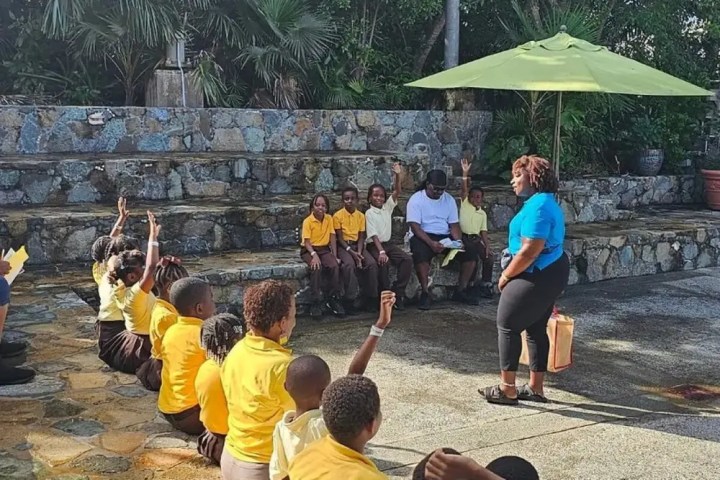 Teacher outdoors with students seated on stone steps and raised hands.