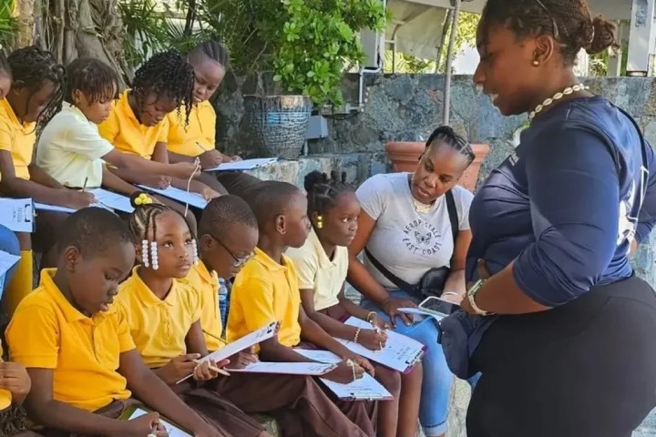 Teacher instructing children in yellow uniforms outdoors.